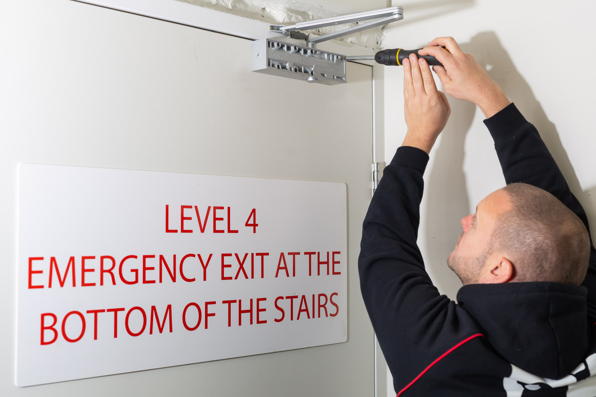 Installing a commercial-grade door closer near an emergency exit, Manningham Medical Centre
